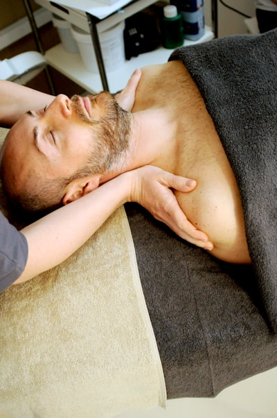 Bearded man covered by the black towel is enjoying shoulder massage