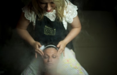 Massage therapist wearing white shirt and black apron is performing head massage