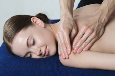 Woman is relaxing on the blue towel while being massaged on the shoulder