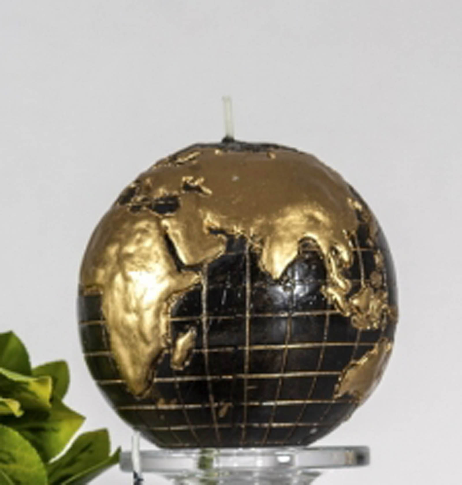 Black and gold globe candle sitting on the glass coaster with the flower leaves in the background