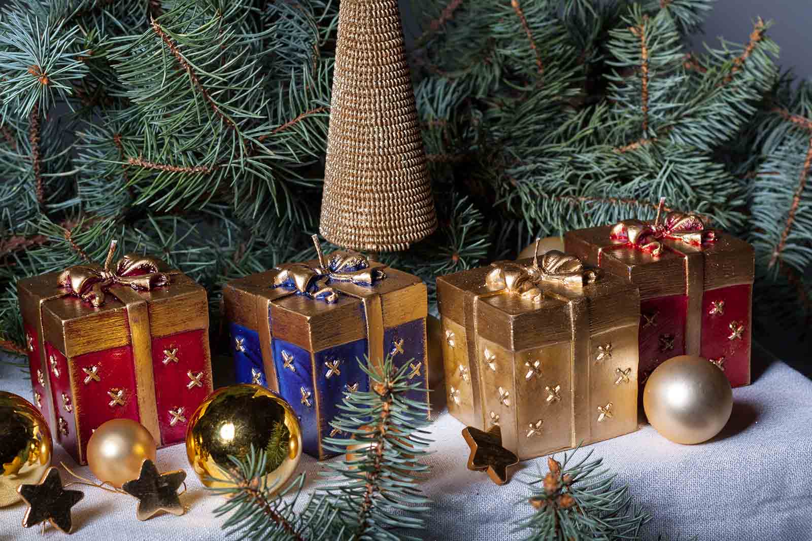 Four candles shaped as a Christmas gift box surrounded by pine leaves and Christmas bubbles