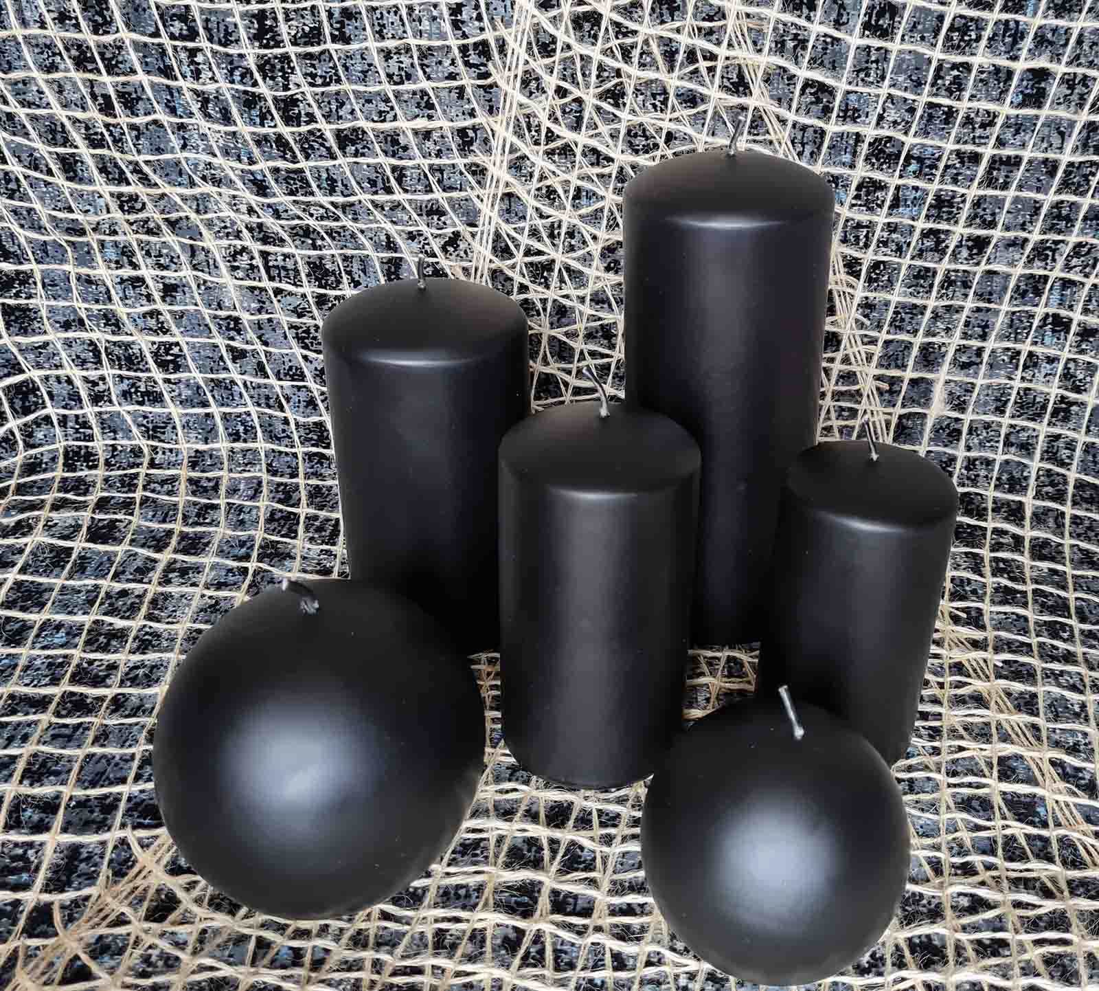 Four pillar and two round black mat candles surrounded by the decorative net on the black background