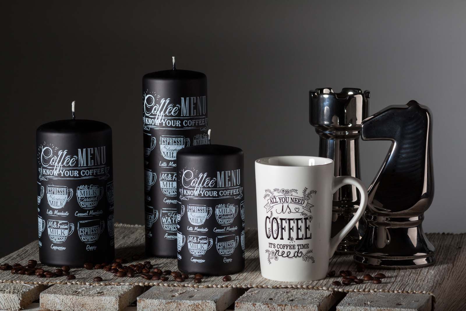 Three pillar candles with Coffee inscription sitting on the wooden table beside coffee mug and two chess figures