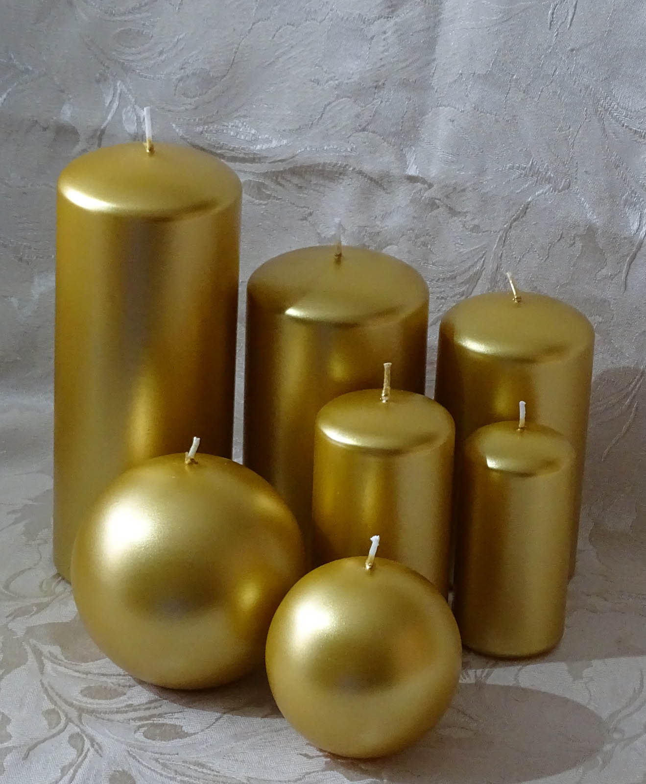 Five pillar and two round candles in gold colour sitting on the cream and silver cable cloth