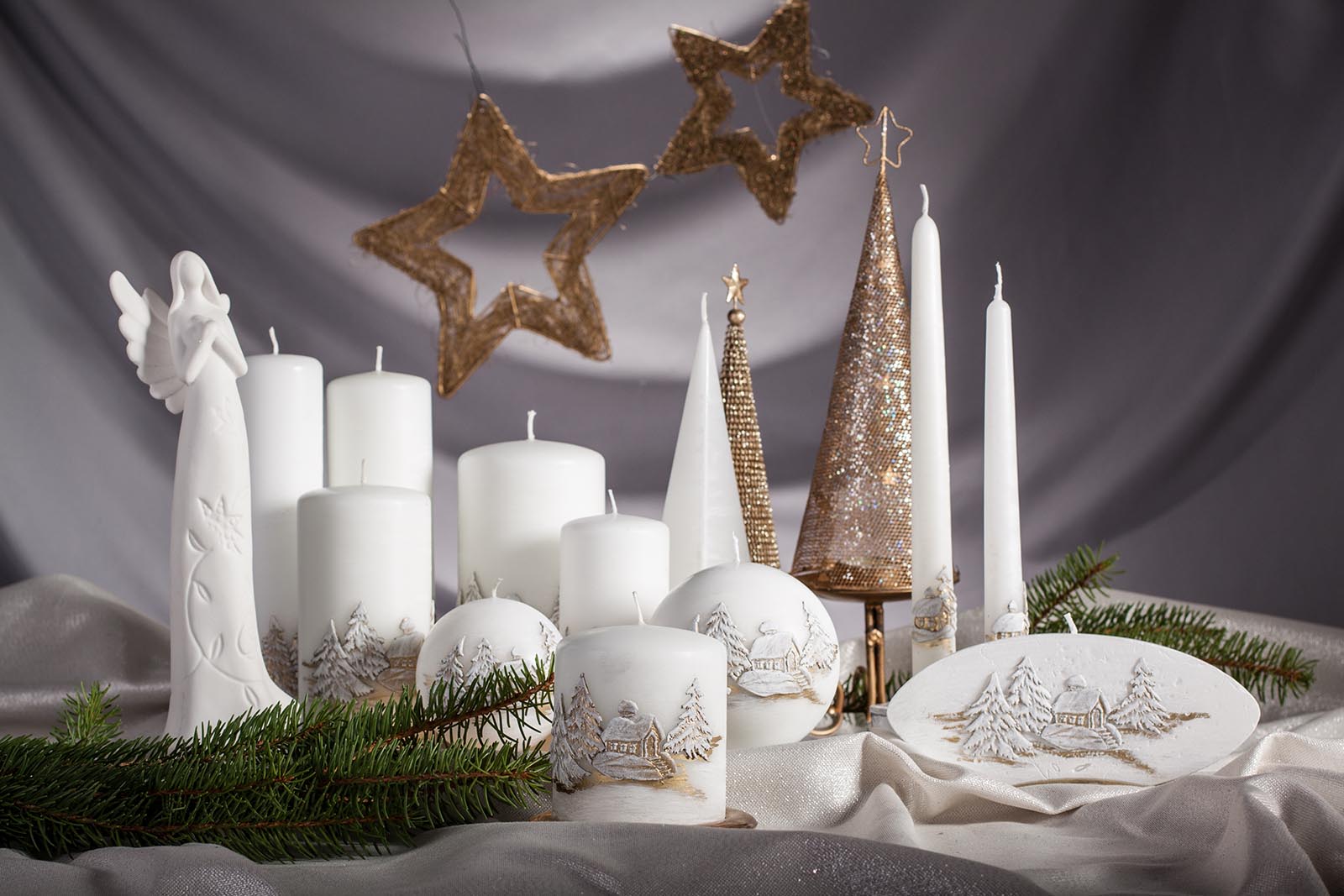 Set of winter themed candles on the white table cloth with Christmas decorations in the background and an angel figurine