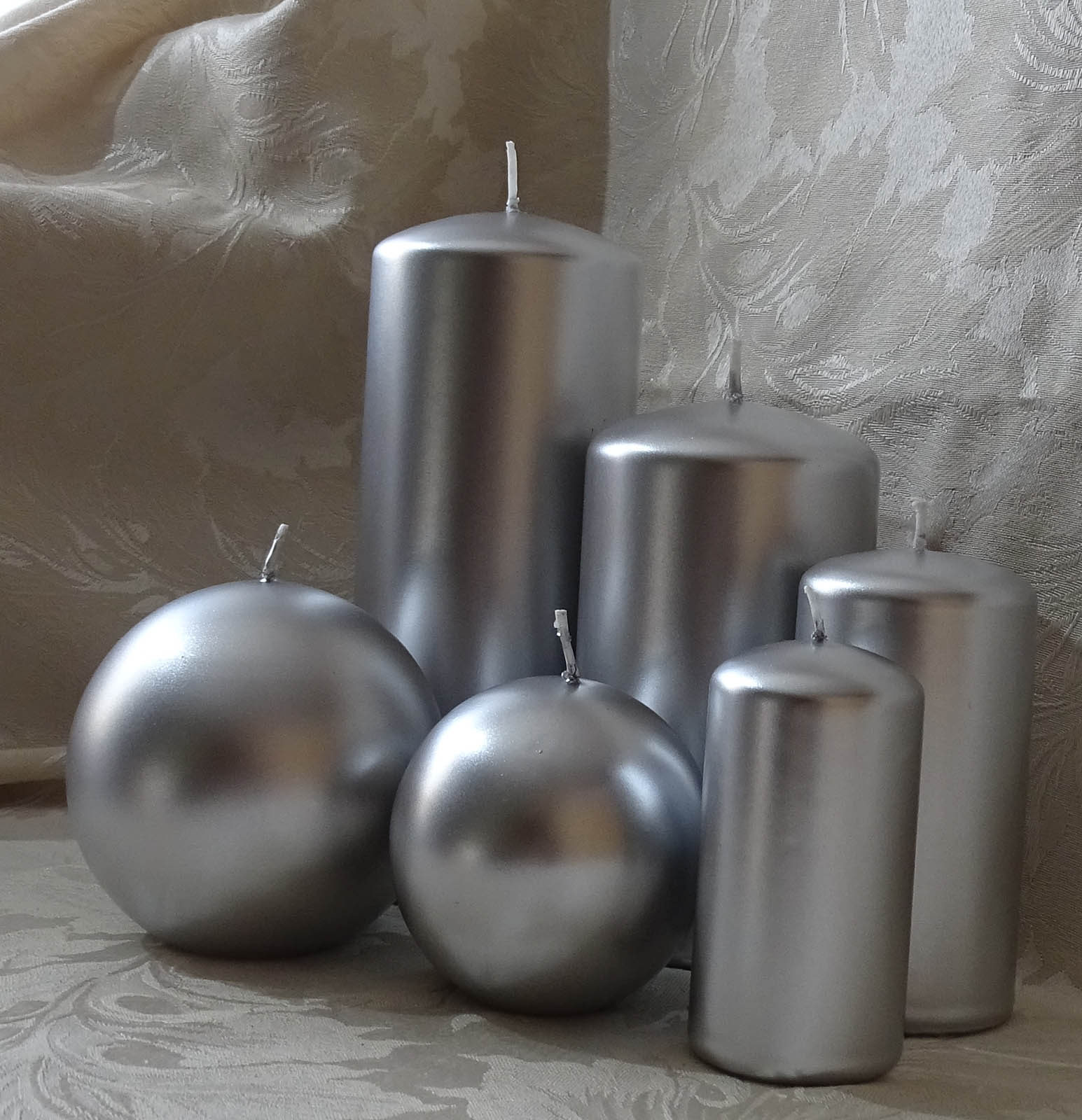 Five pillar and two round candles in silver colour sitting on the cream and silver cable cloth