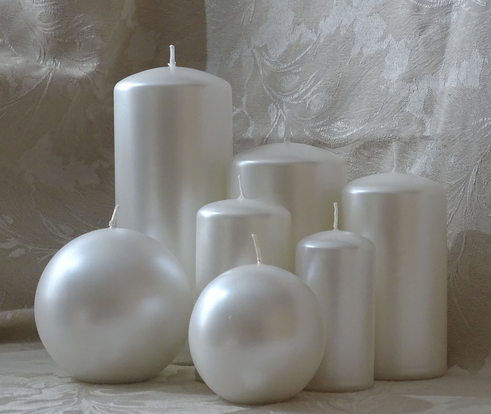 Five pillar and two round candles in pear colour sitting on the cream and silver cable cloth