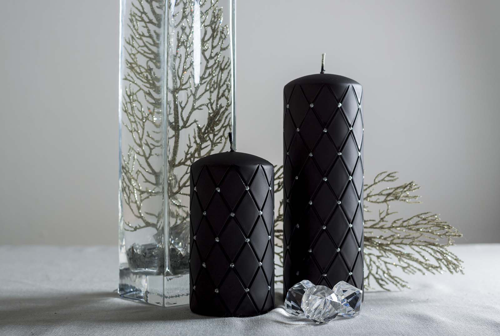 Two black  pillar candles with diamond pattern beside tall flower vase and three diamonds