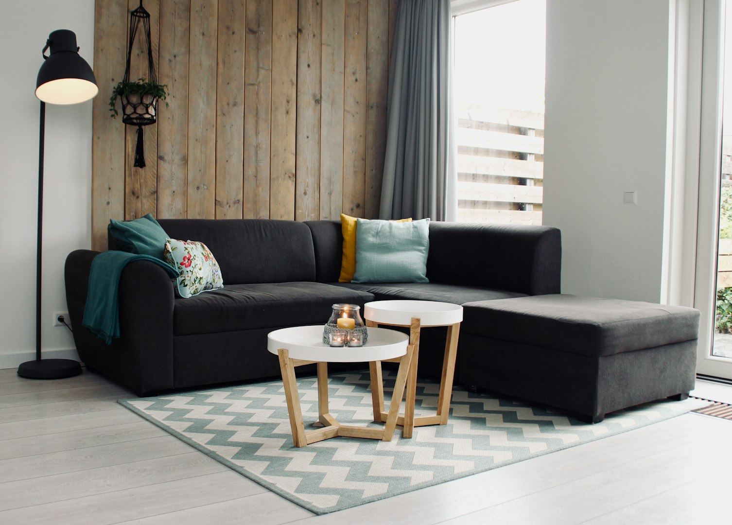 Cozy Livingroom with large black sofa, white coffee table with the candle in the jar and black standing lamp beside wood cladded wall 