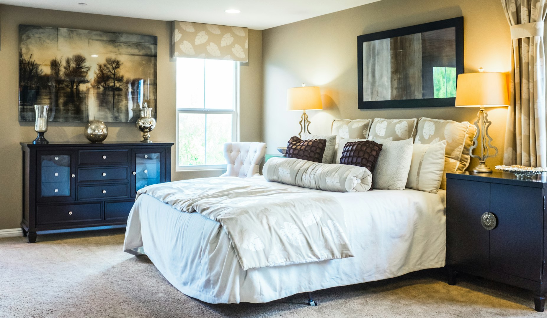 Bedroom with the large bed covered with multiple pillows, black furniture and the mirror in the black frame